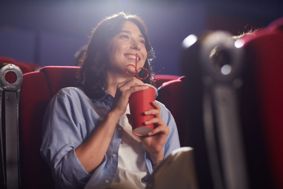 Mulher segurando copo vermelho e sorrindo em uma sala de cinema